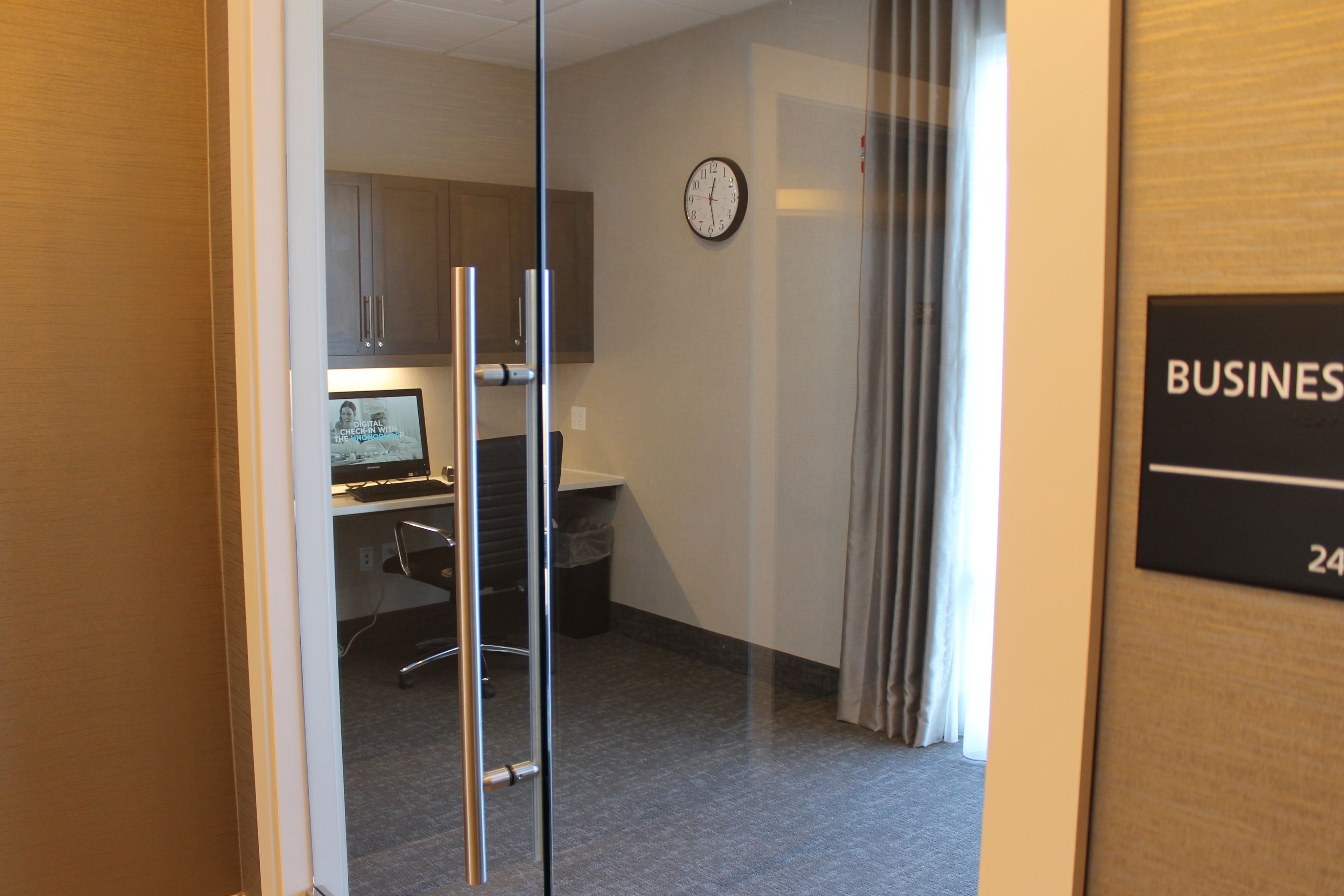 A hotel room with a glass door leading to a kitchenette, a clock on the wall, and a sign indicating the room number.