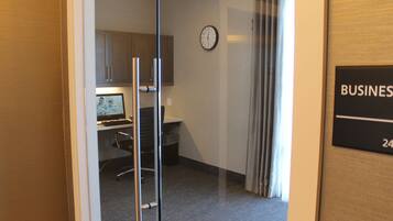 A hotel room with a glass door leading to a kitchenette, a clock on the wall, and a sign indicating the room number.