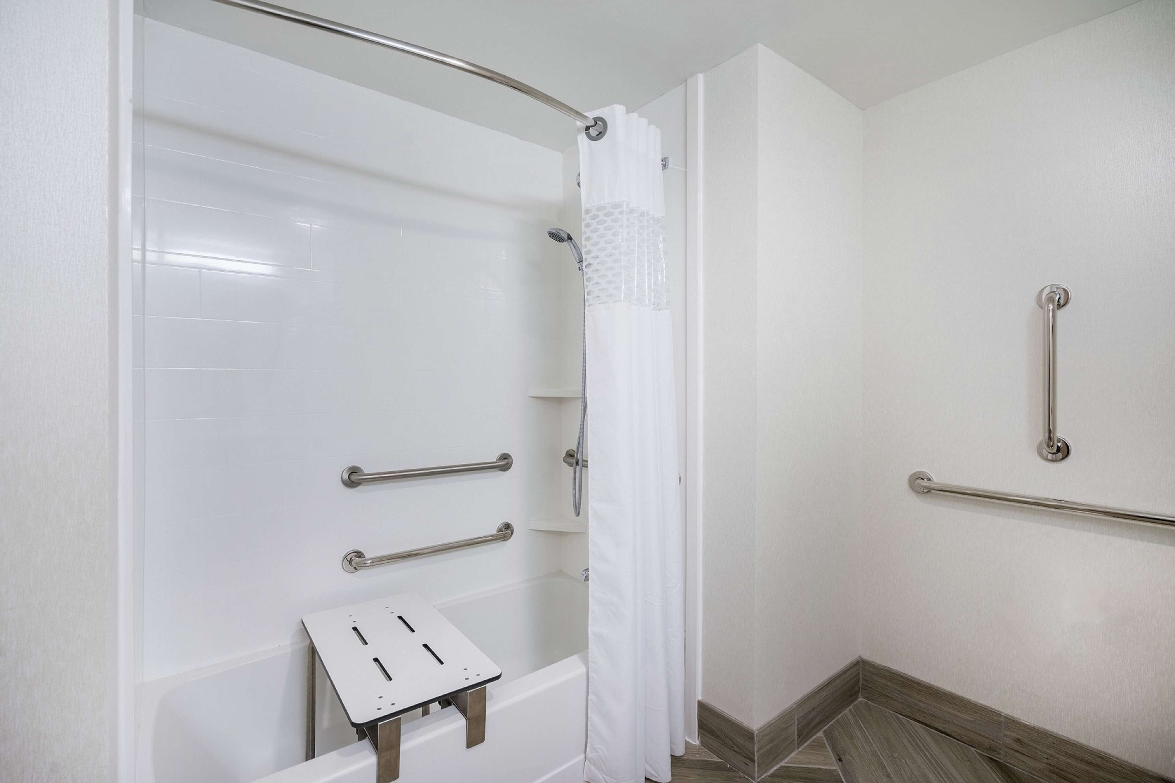 A bathroom with a white bathtub, a shower with a white curtain, and a grab bar on the wall.
