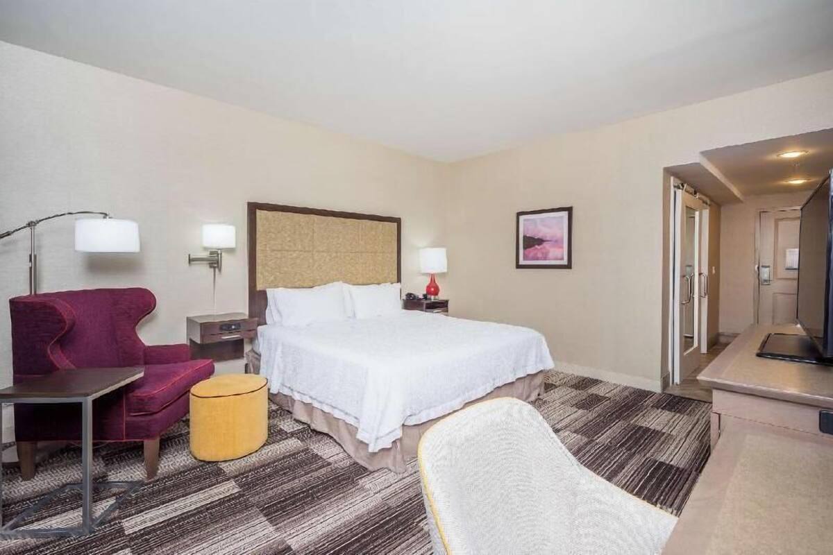 A hotel room with a bed, a desk, a chair, a lamp, and a television.
