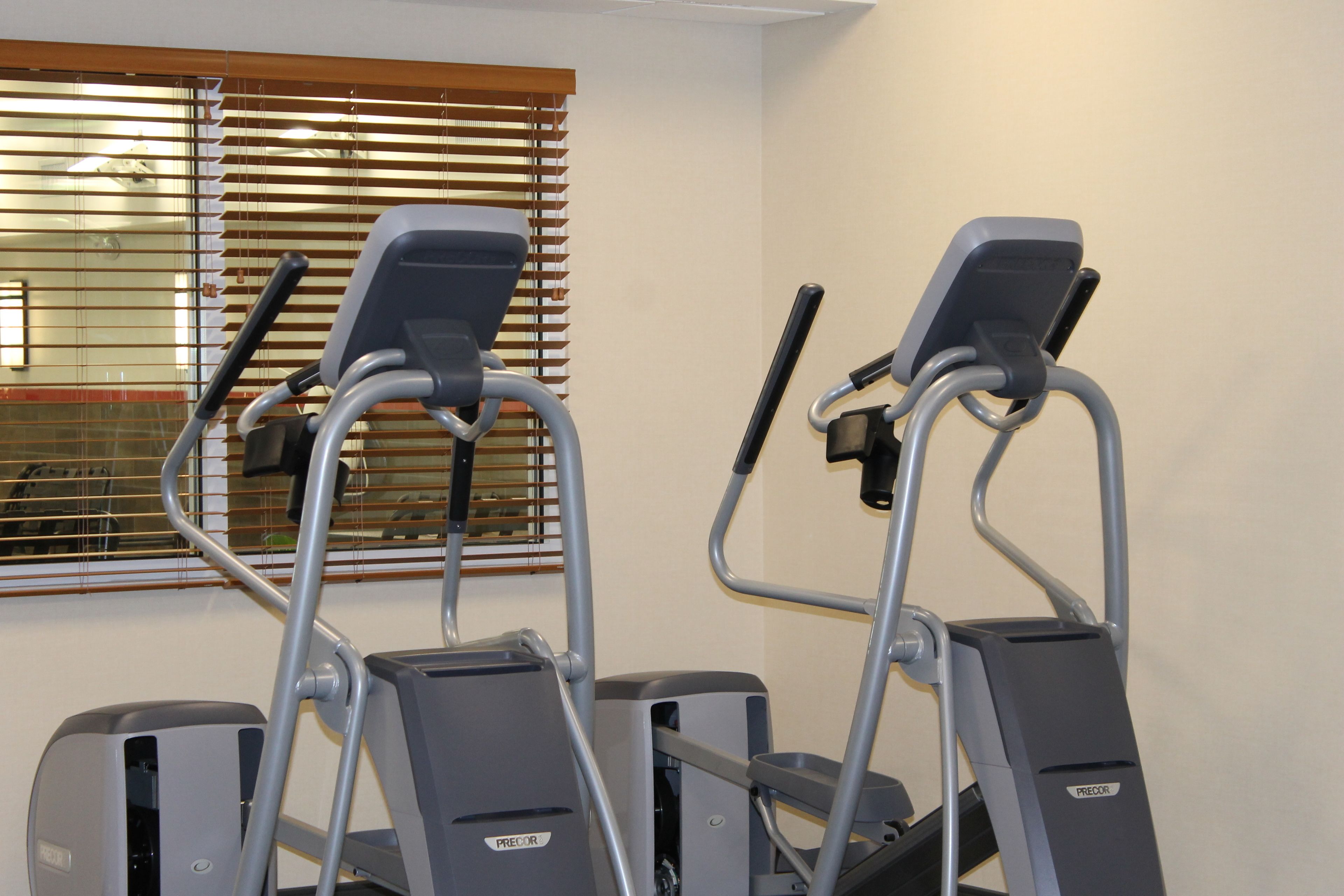 Two stationary bikes in a room with a window with blinds.