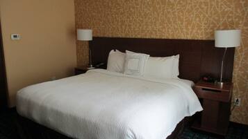 A hotel room with a large bed, two bedside tables with lamps, a headboard, and patterned wallpaper.