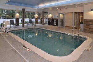 Una piscina interior con agua cristalina, rodeada de sillones de descanso y una zona de recepción.
