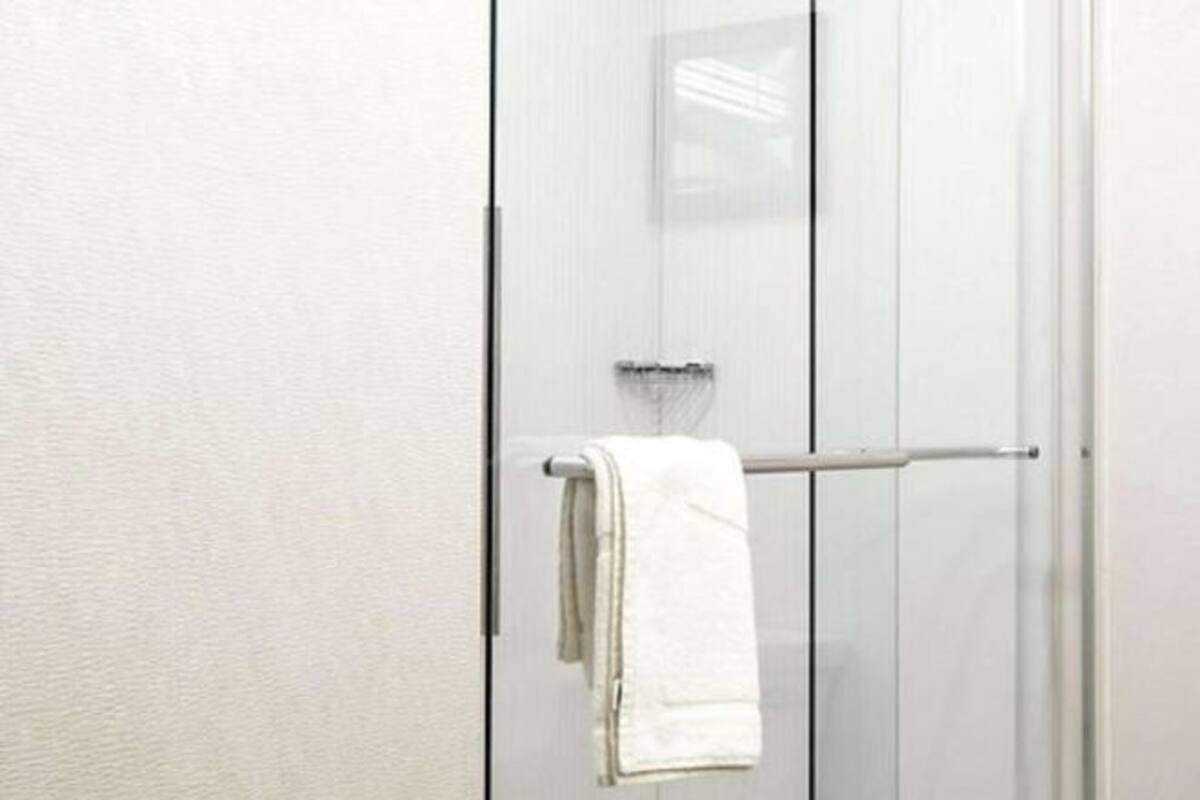 A bathroom with a glass shower door, a towel rack, and a white towel hanging on the door.
