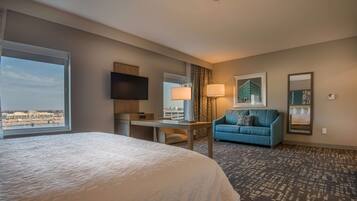 Habitación de hotel con una cama grande, un escritorio, un sofá azul, un televisor y vistas a la ciudad.