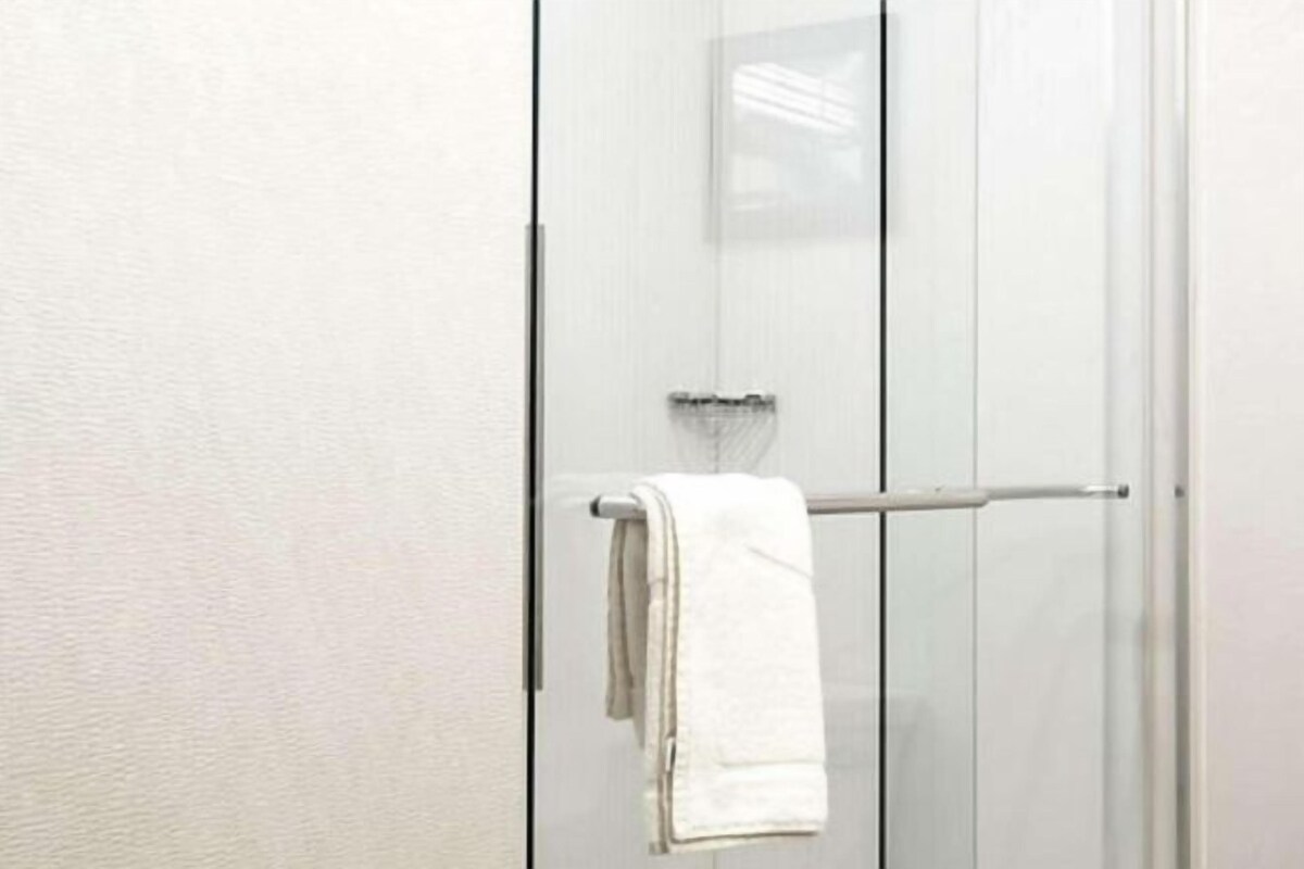 A bathroom with a glass shower door, a towel rack, and a white towel hanging on the door.