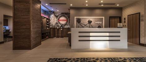 A modern reception area with a wooden reception desk, a 'Treats' sign, and a 'Enjoy' poster on the wall.