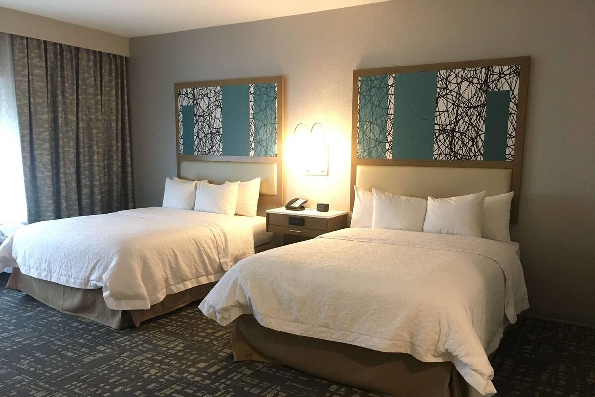 Une chambre d’hôtel avec deux lits, une table de chevet avec un téléphone et une œuvre d’art murale.