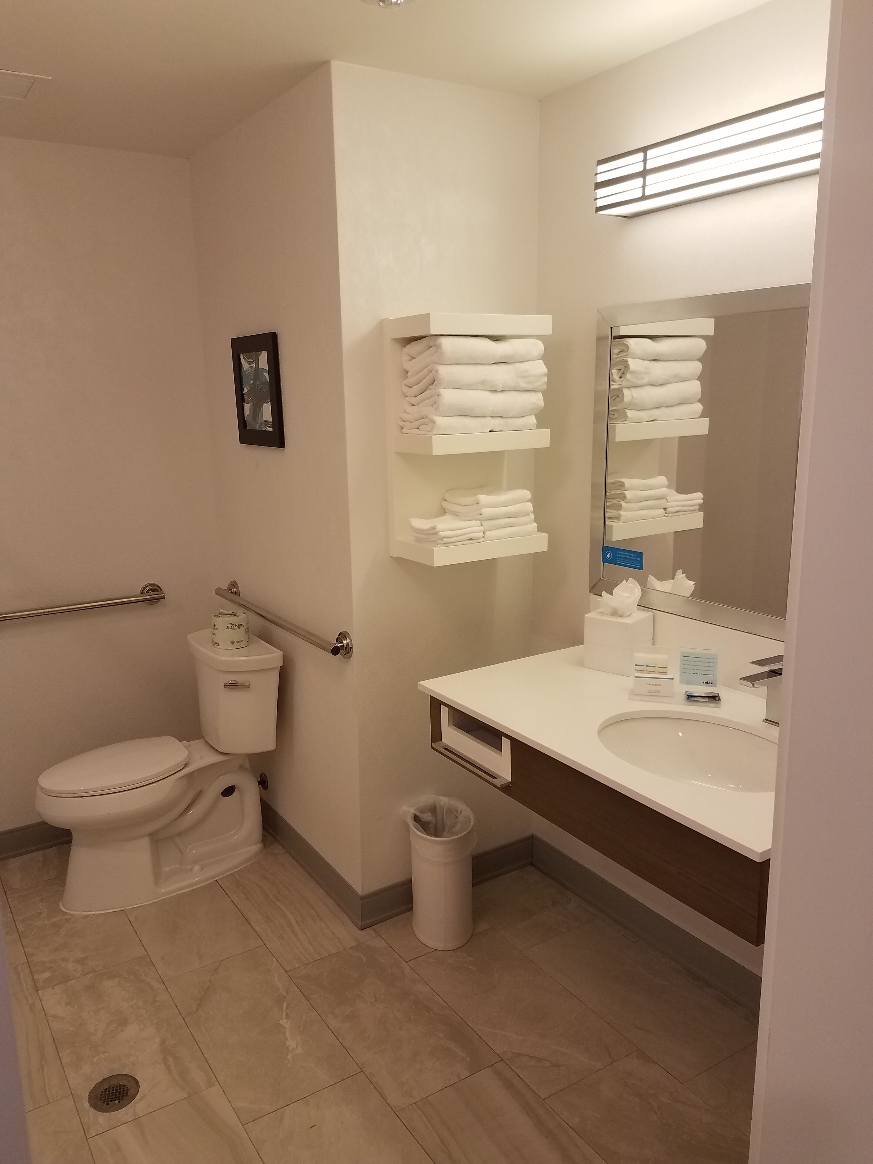 A hotel bathroom with a toilet, sink, and towel racks.