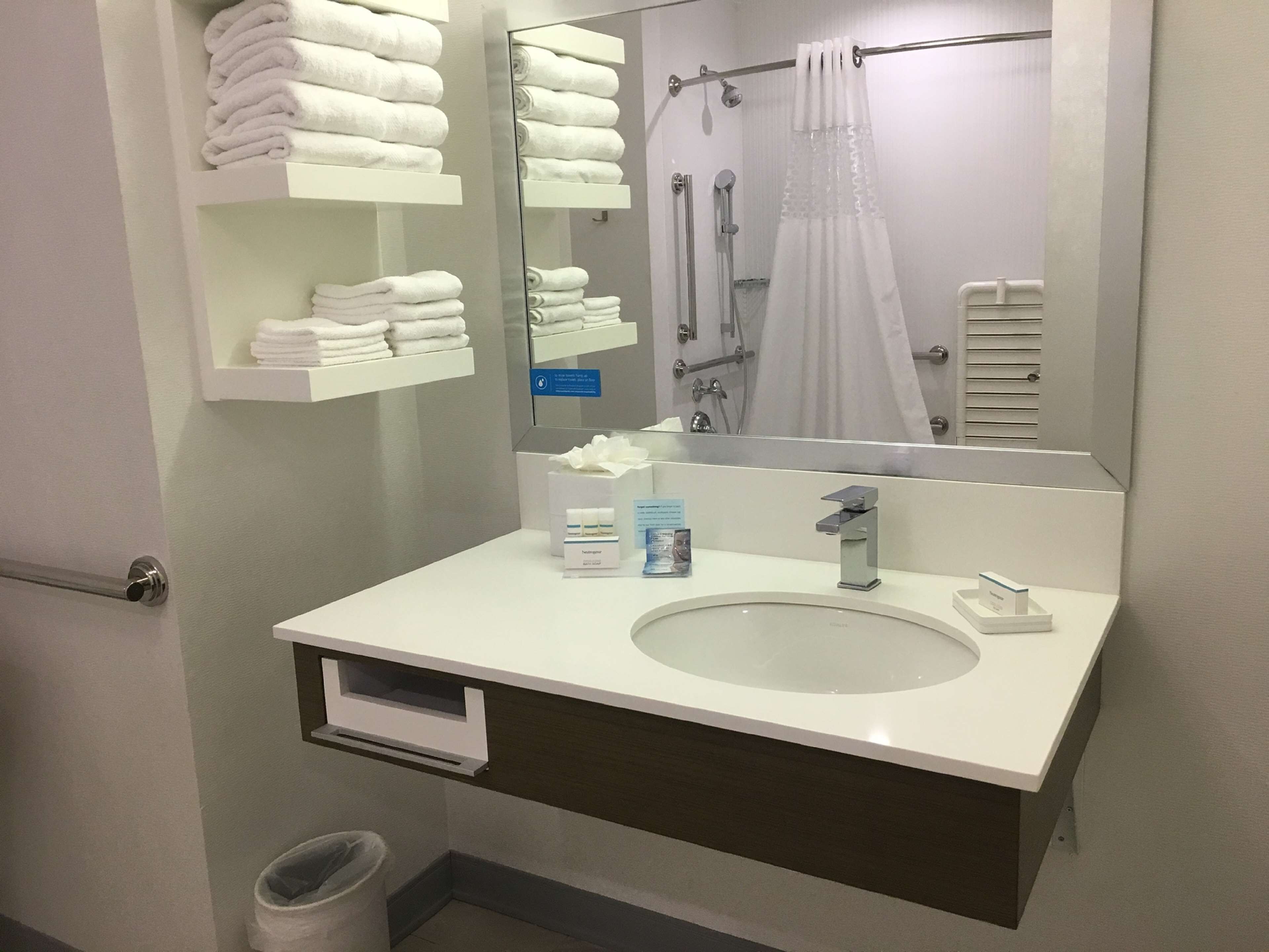 Un baño moderno con un lavabo blanco, un espejo grande y un perchero con toallas dobladas.