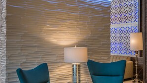 A modern lobby with a textured wall, two teal armchairs, a round table, and a decorative wall panel. - Hampton Inn & Suites Dallas-The Colony, TX (The Colony)