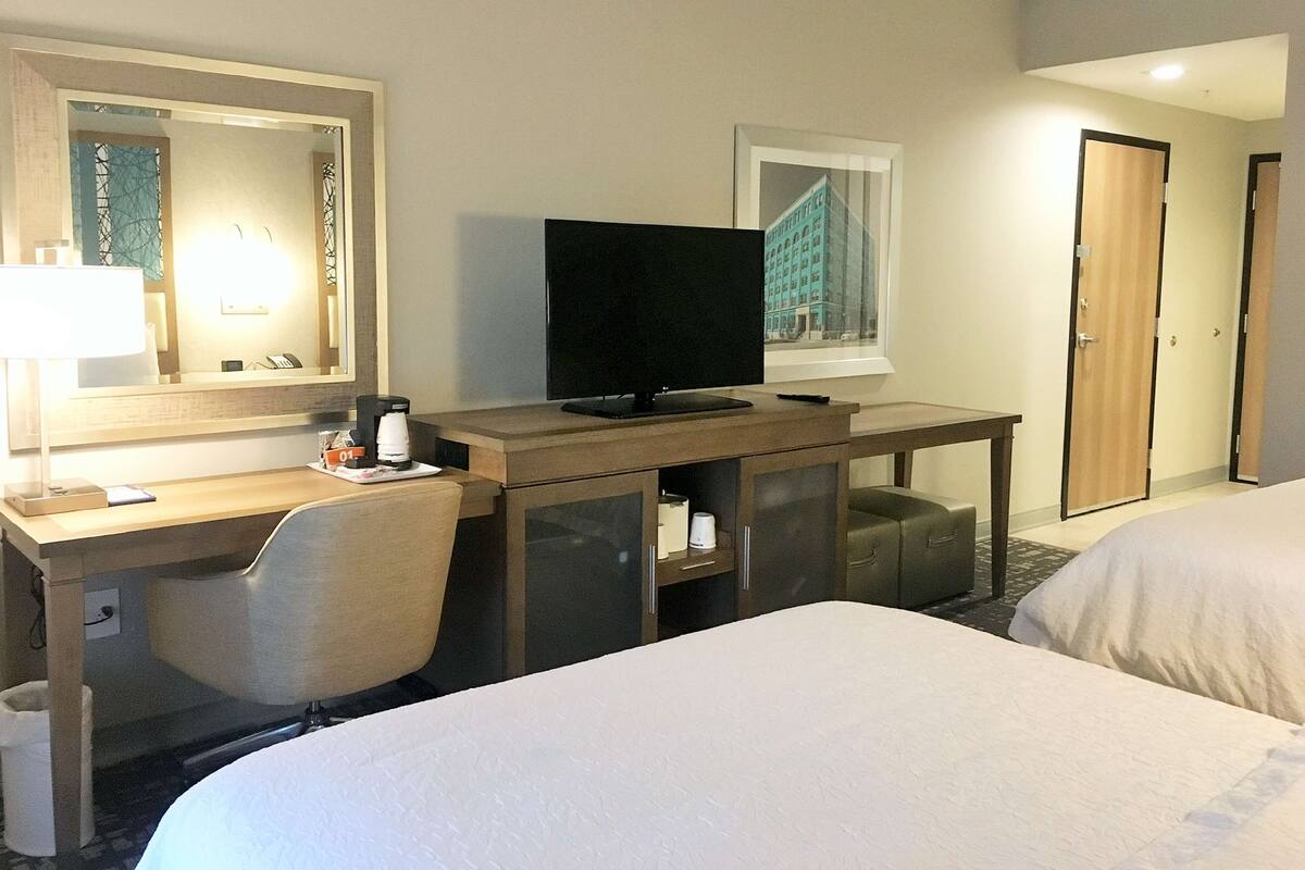 Une chambre d’hôtel avec un lit, un bureau avec un ordinateur, une chaise, une télévision et un miroir.