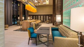 A modern hotel lobby with a dining area, seating, and decorative lighting. - Hampton Inn & Suites Dallas-The Colony, TX (The Colony)