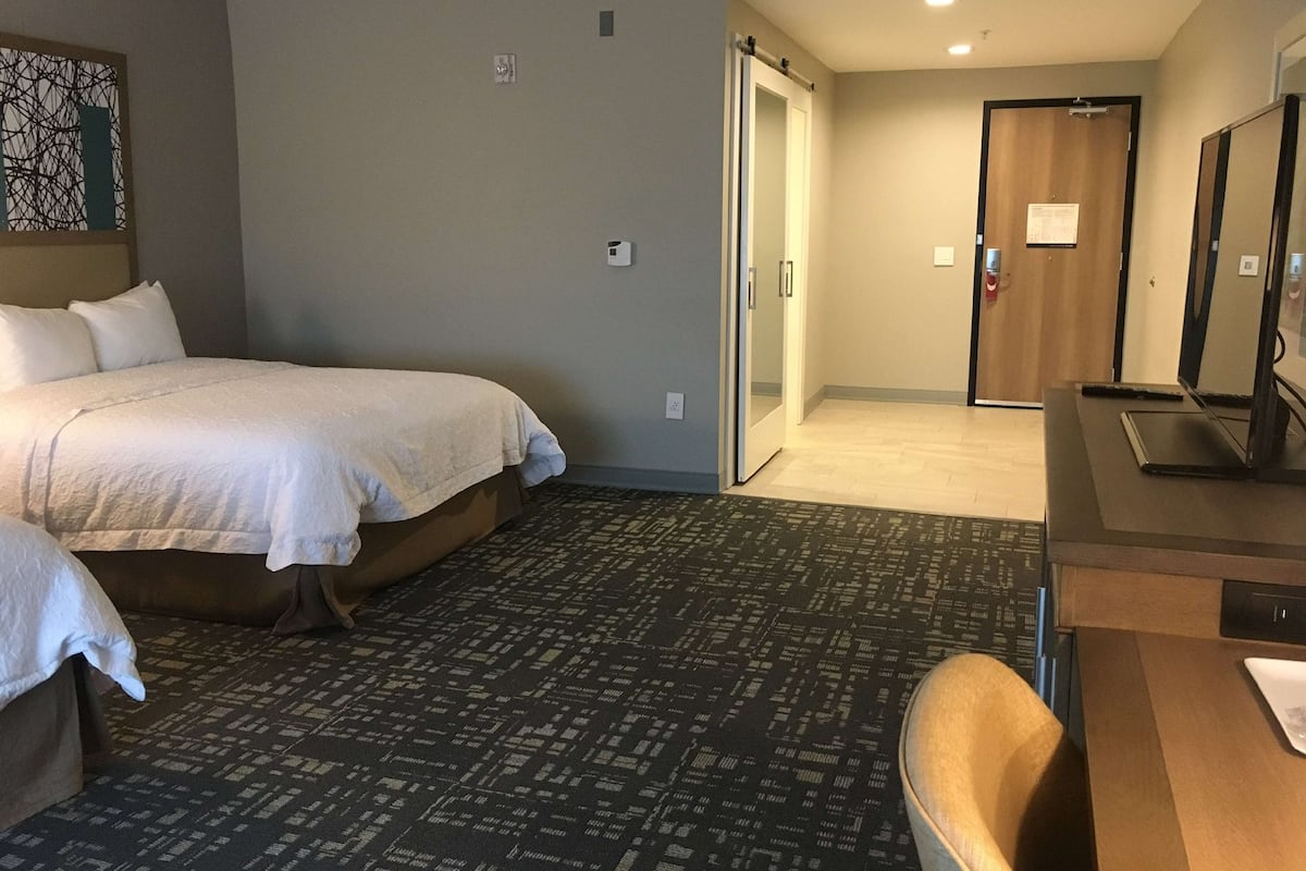 Une chambre d’hôtel avec un lit, un bureau et une chaise. Une porte donne accès à une autre pièce.
