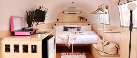 Een compacte slaapkamer met een bed, een bureau met een computer, een kleine plant en een raam.