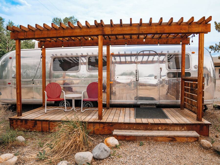 A camper with a wooden deck and two chairs.
