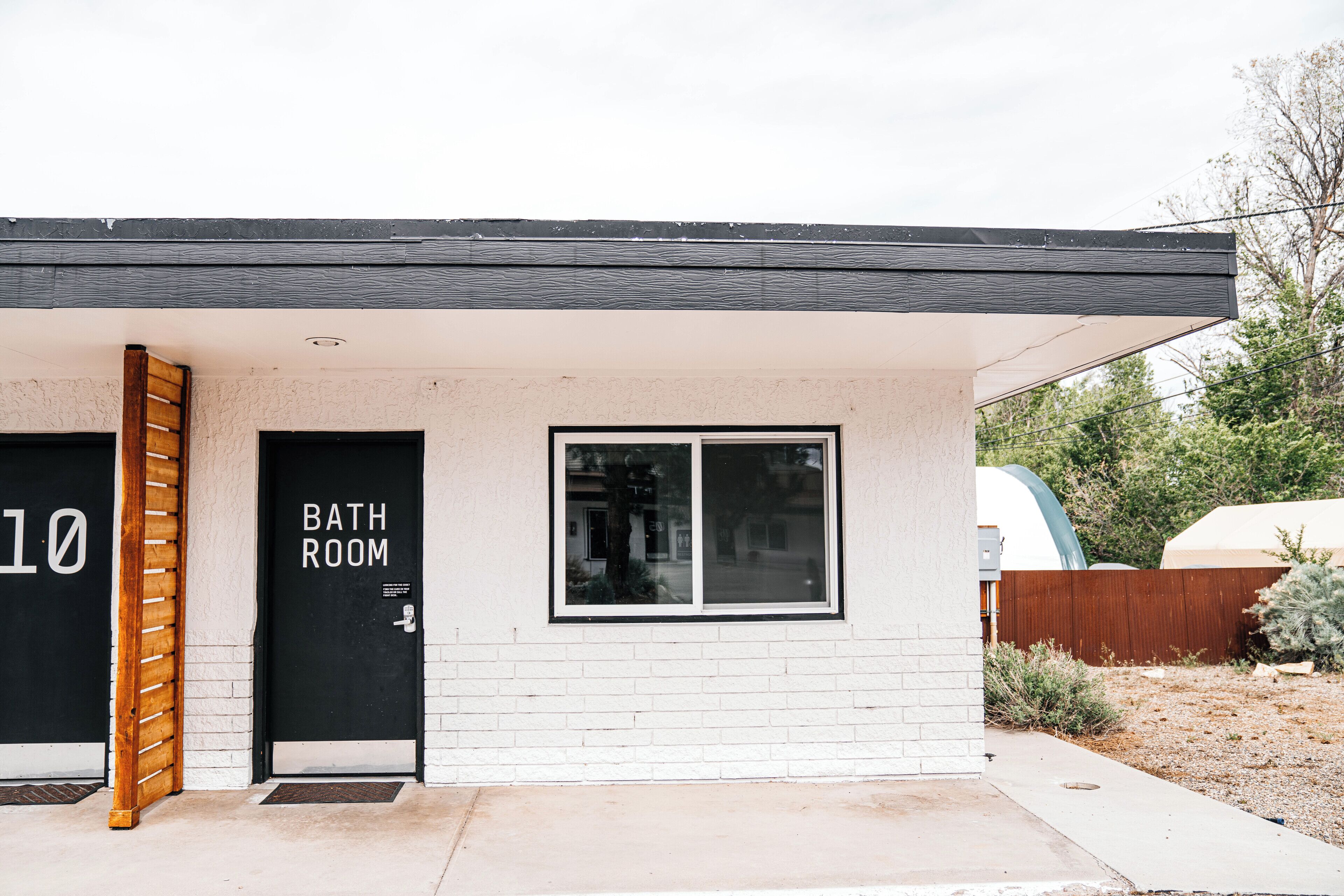 A building with a white exterior, a black door labeled "BATHROOM," and a window.