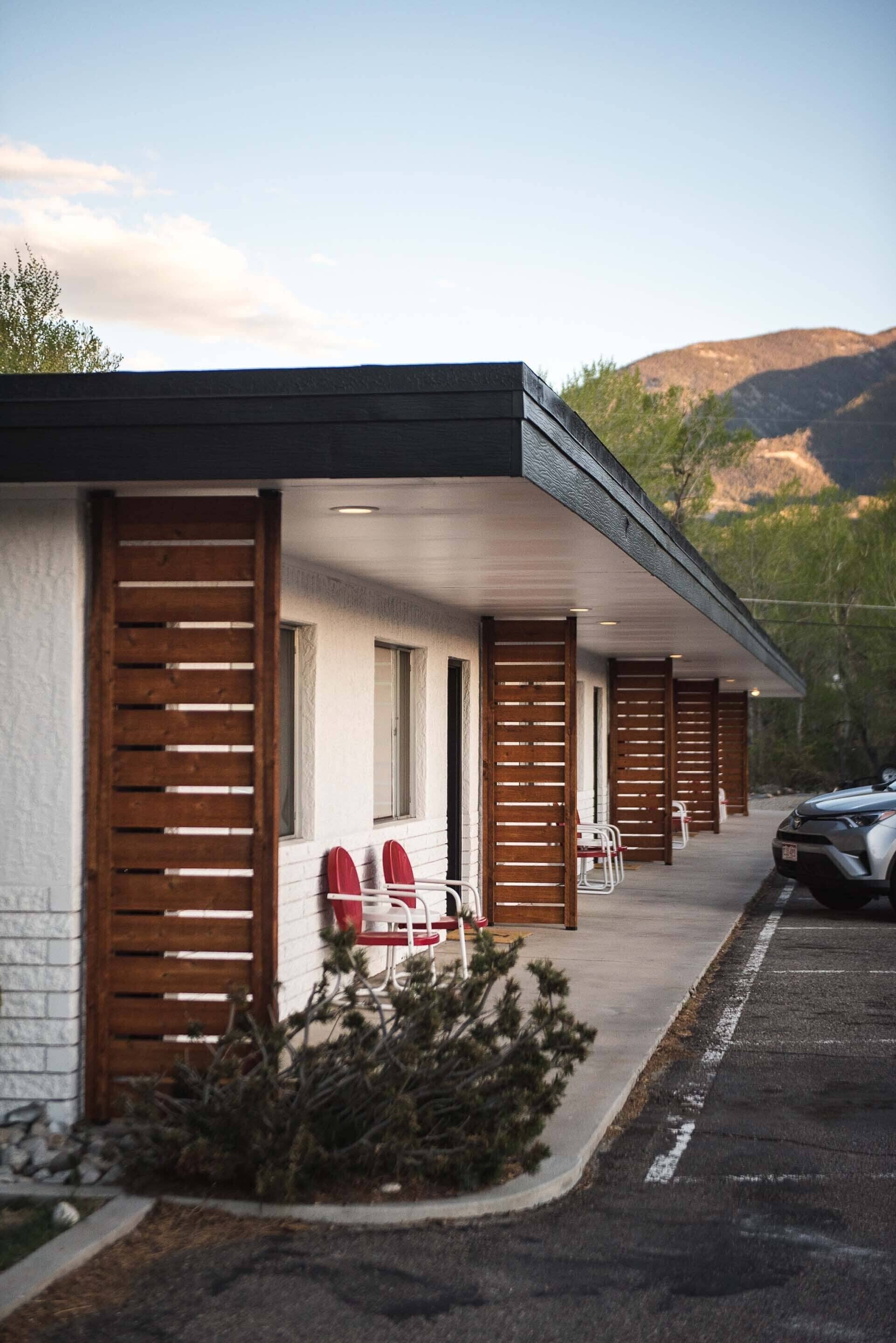 Un motel con un porche cubierto, zona de estacionamiento y montañas al fondo.