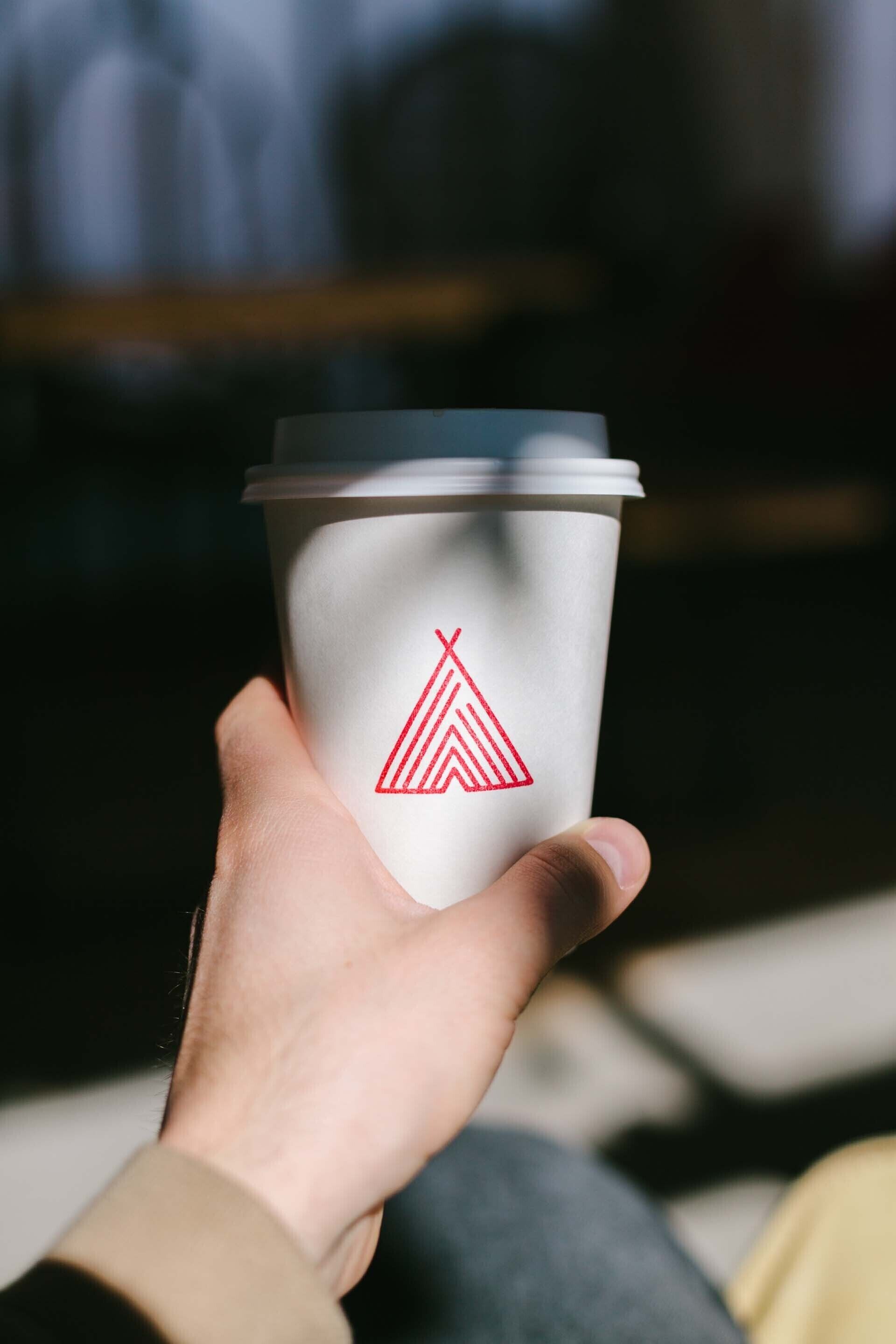 A hand holding a white paper cup with a red logo.