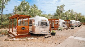 A row of vintage trailers with wooden porches, each with a small porch area and a bench. - The Amigo Motor Lodge (Salida)
