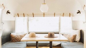 A cozy interior with a table and bench seating, a hanging light fixture, and a window with curtains. - The Amigo Motor Lodge (Salida)