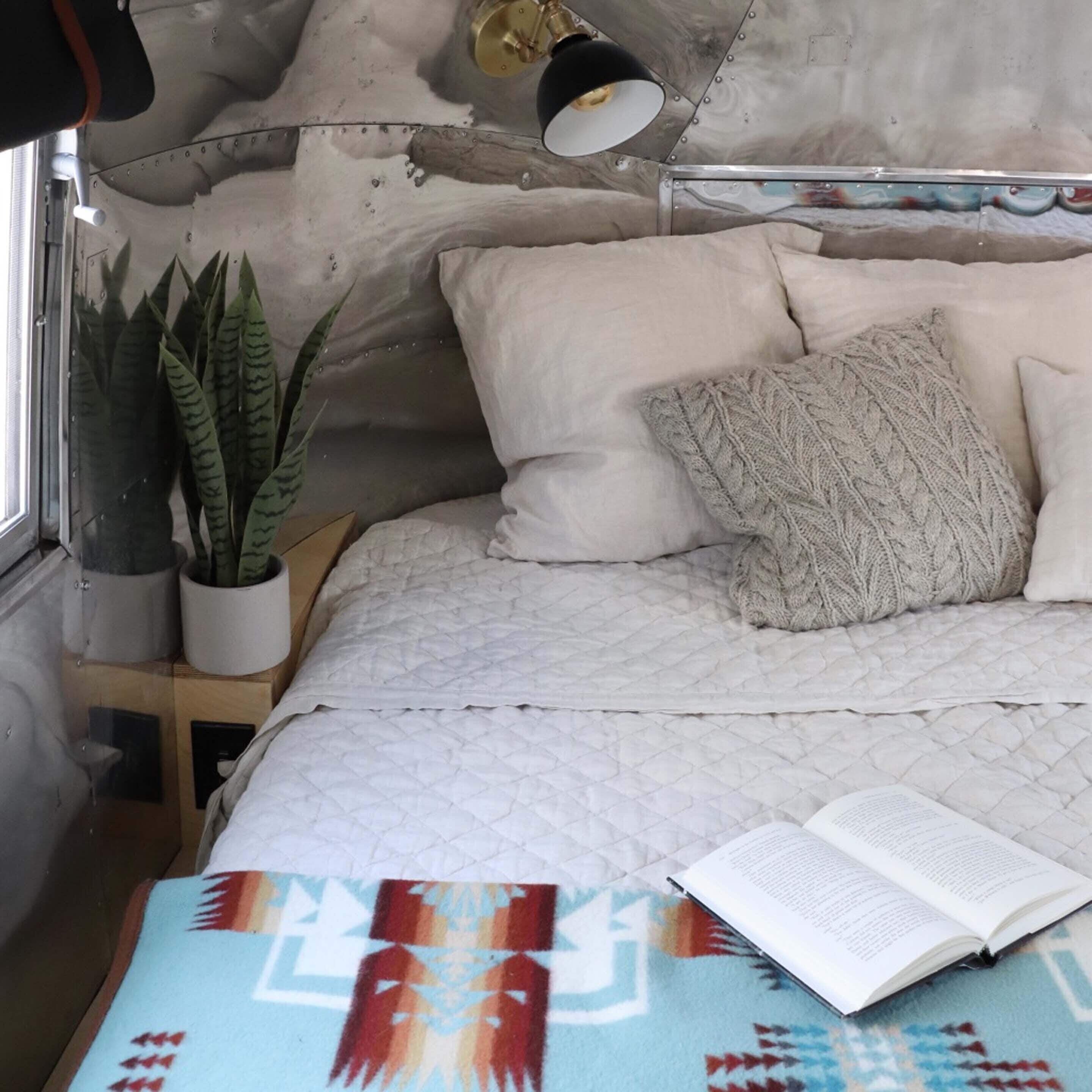 A bed with a quilted blanket, a book, and a potted plant.