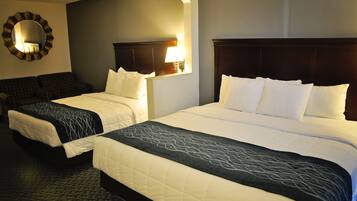 A hotel room with two beds, a large mirror, and a wall-mounted lamp.