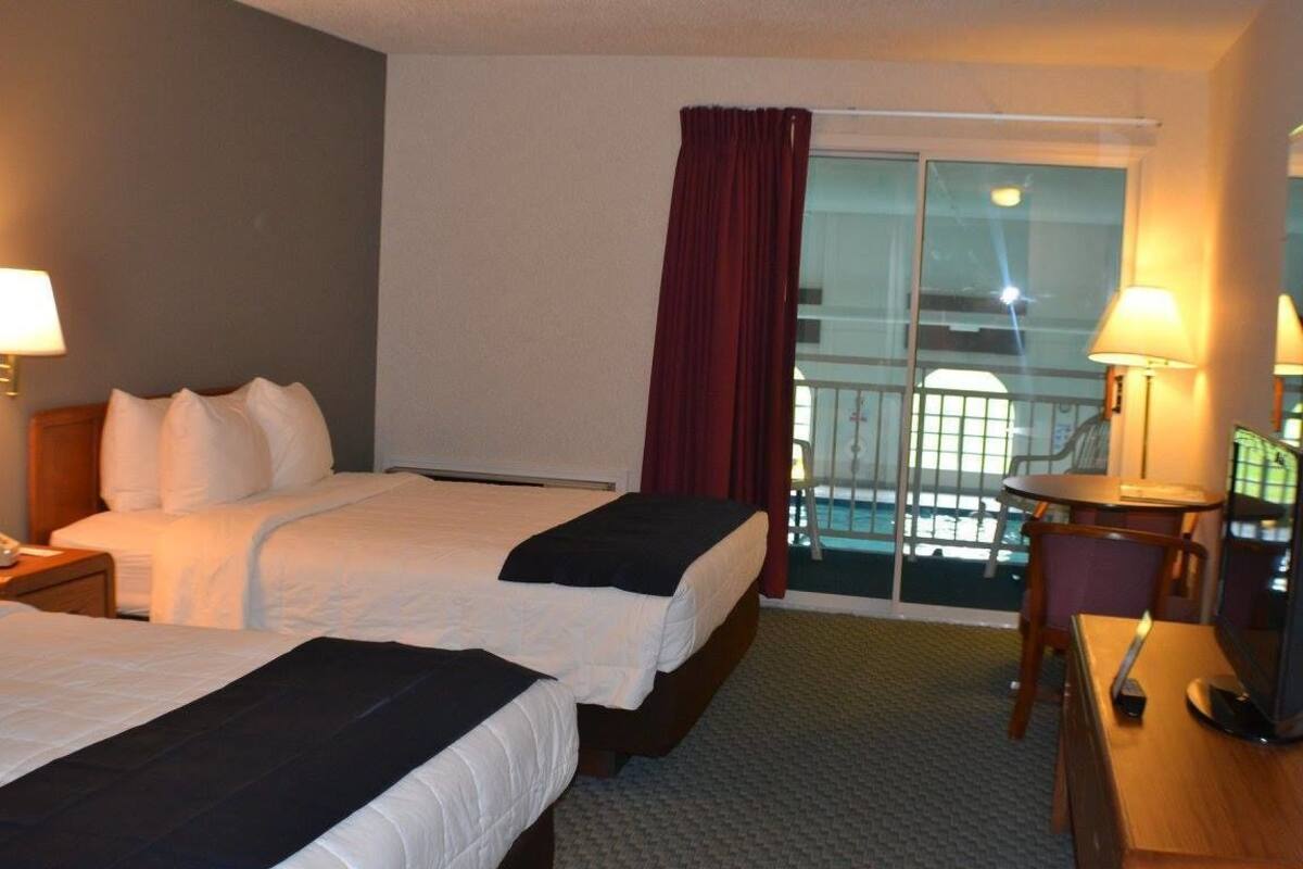Une chambre d’hôtel avec deux lits, un bureau avec une chaise, une télévision et un balcon offrant une vue sur la ville.