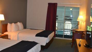 A hotel room with two beds, a desk with a chair, a TV, and a balcony with a view of the city.