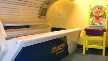Una cama bronceadora con decoración azul y blanca, una pared amarilla y una pequeña silla con un cuadro de colores.