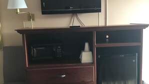A hotel room with a TV mounted on the wall, a wooden desk with drawers, a microwave, and a small refrigerator. - Redwood Inn (Gadsden)