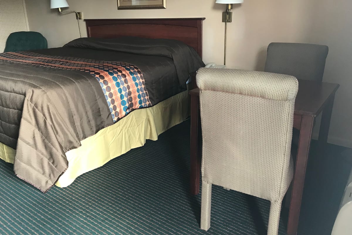 A hotel room with a bed, a chair, a desk, and two wall lamps.