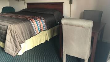 A hotel room with a bed, a chair, a desk, and two wall lamps.