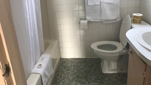 A bathroom with a toilet, a sink, a shower curtain, and a towel rack. - Redwood Inn (Gadsden)