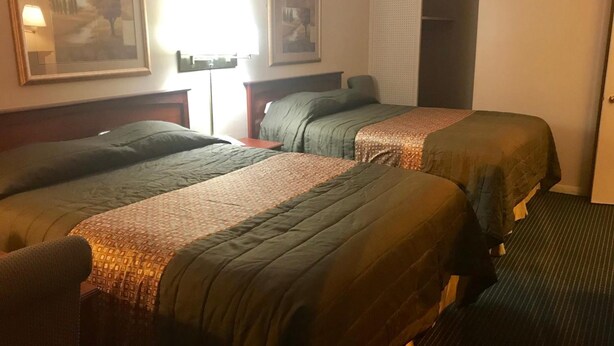 A hotel room with two beds, a nightstand, a lamp, and a door. - Redwood Inn (Gadsden)
