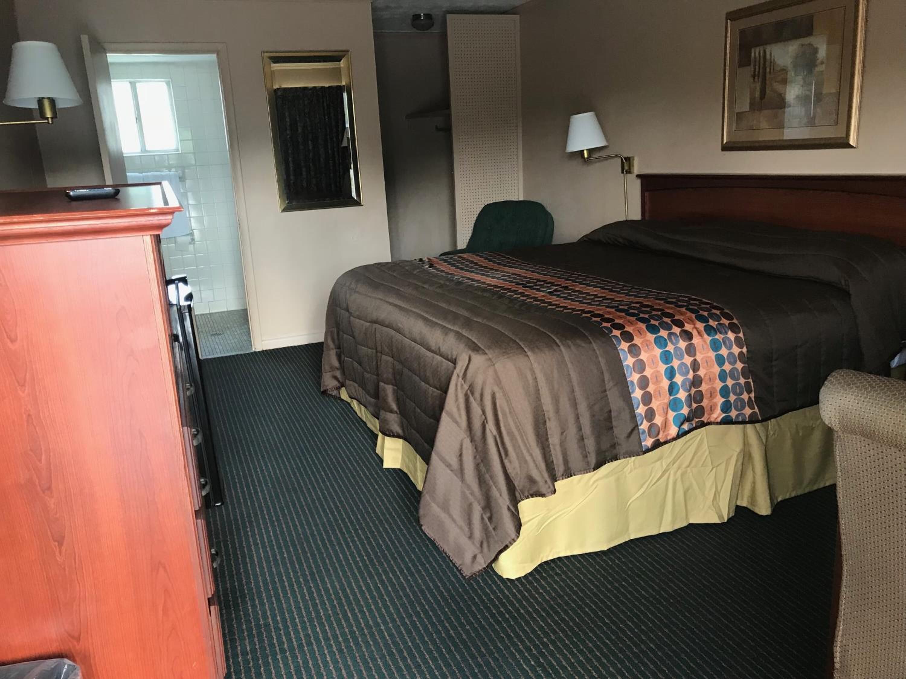 A hotel room with a bed, a desk, a chair, a lamp, and a painting on the wall.
