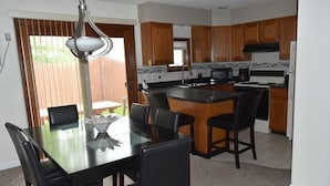 Una cocina moderna con armarios de madera, una isla central y un comedor con mesa y sillas de vidrio.