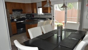 Una cocina moderna con armarios de madera, una isla central y un comedor con mesa negra y sillas blancas.