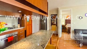 A modern kitchen with granite countertops, wooden cabinets, and a red towel hanging on the oven. - Apartamentos Premium Capital Casino Viña Del Mar (Vina del Mar)
