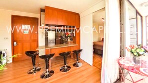 A modern kitchen with wooden cabinets, a stainless steel island, and four black bar stools. - Apartamentos Premium Capital Casino Viña Del Mar (Vina del Mar)