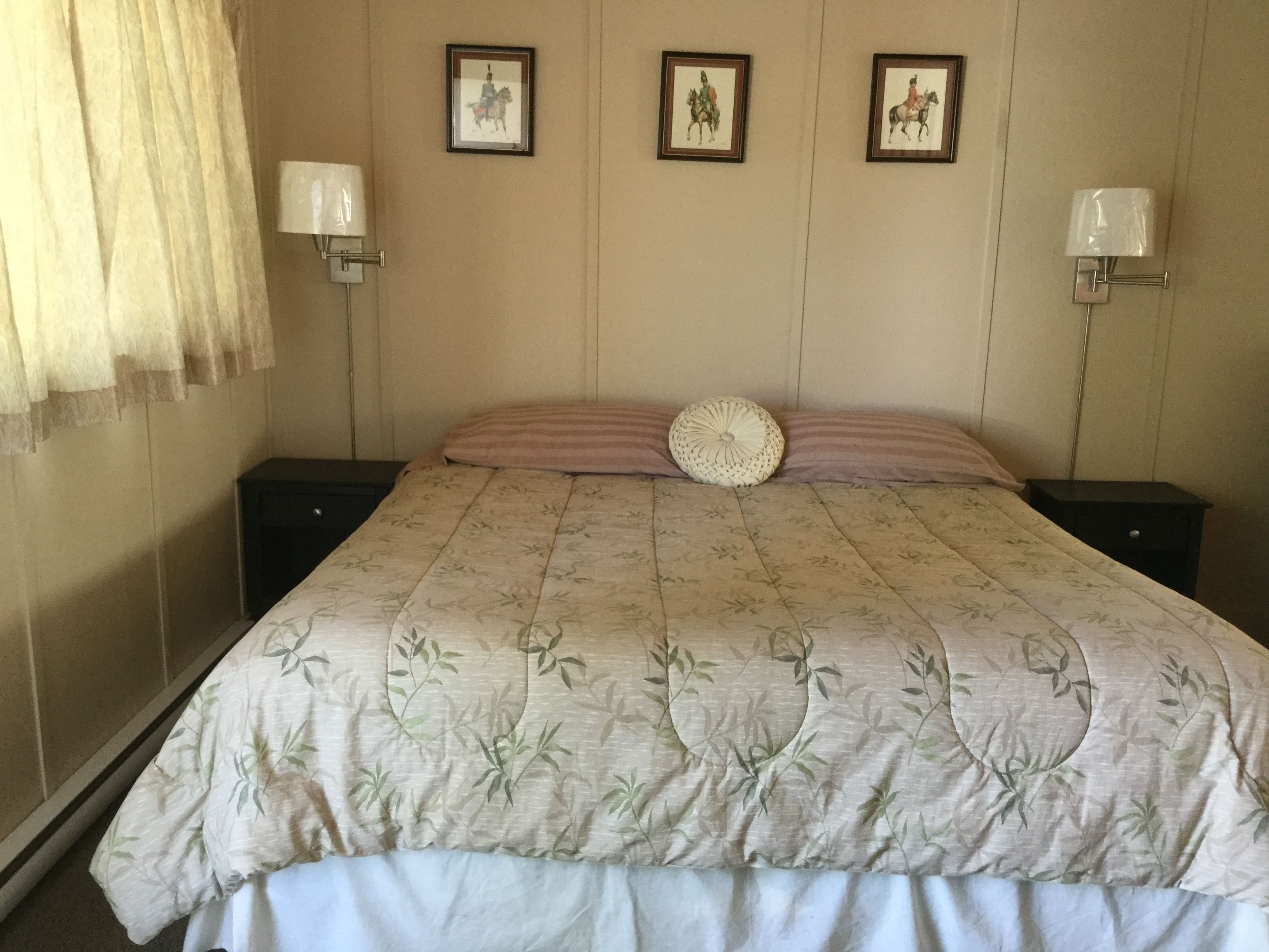A neatly made bed with a floral bedspread, two wall-mounted lamps, and three framed pictures on the wall.