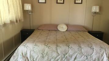 A neatly made bed with a floral bedspread, two wall-mounted lamps, and three framed pictures on the wall.
