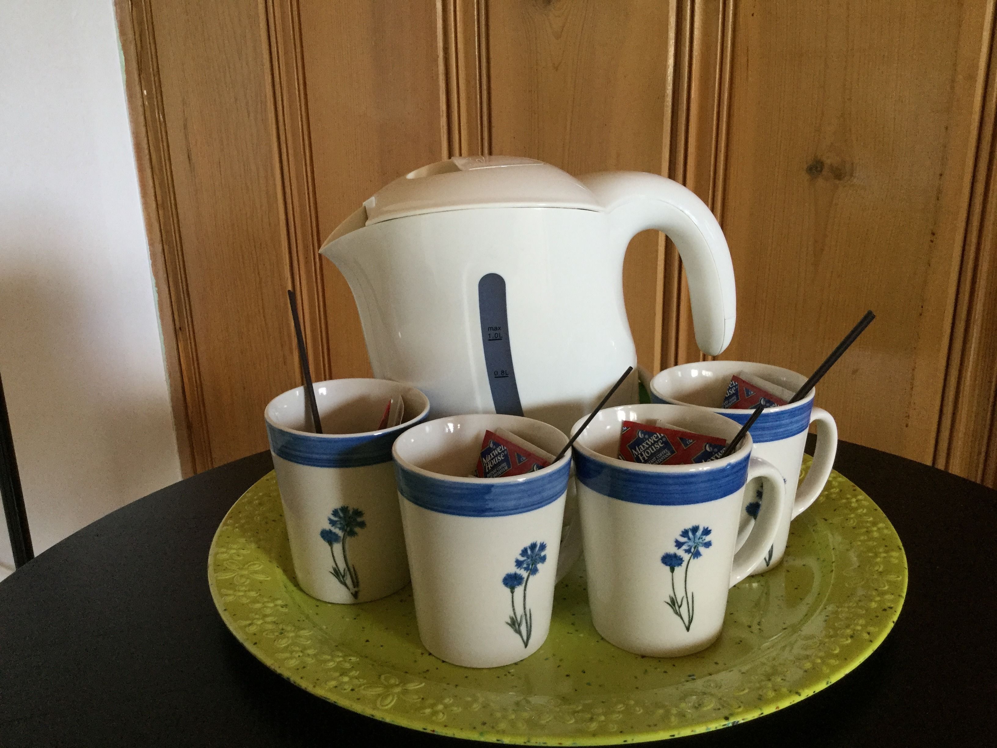 Una mesa con un plato verde que sostiene cuatro tazas blancas con diseños florales azules y una tetera blanca con asa azul.