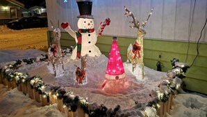 A snowman with a black top hat and scarf, a pink cone, and a reindeer with a red bow.