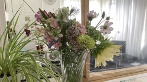 A room with a large window, a clock on the wall, and a floral arrangement on a table.