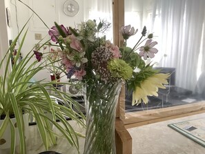 A room with a large window, a clock on the wall, and a floral arrangement on a table.