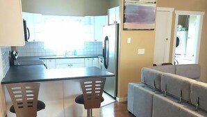 A compact kitchen with a dining area, a gray sofa, and a washing machine in the background. - Cedars Motel (Princeton)