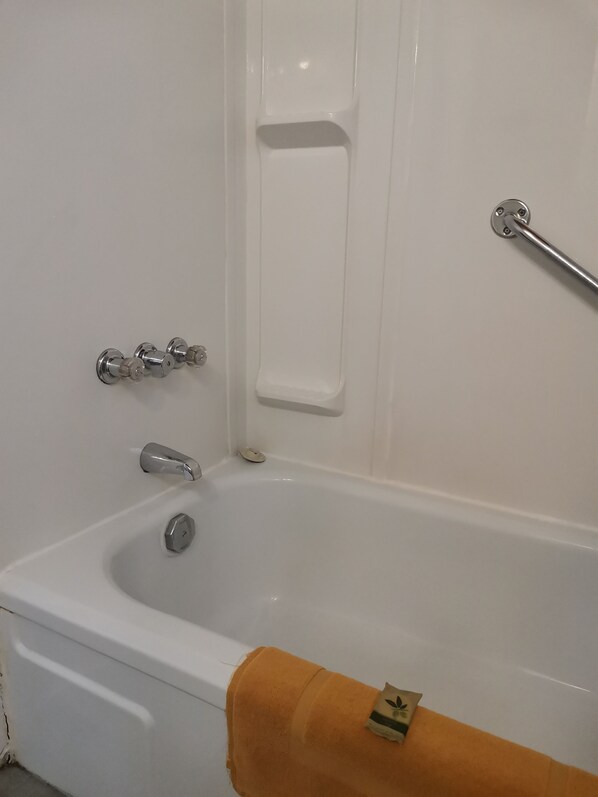 Una bañera blanca con cabezal de ducha manual, toallero y barra de apoyo.