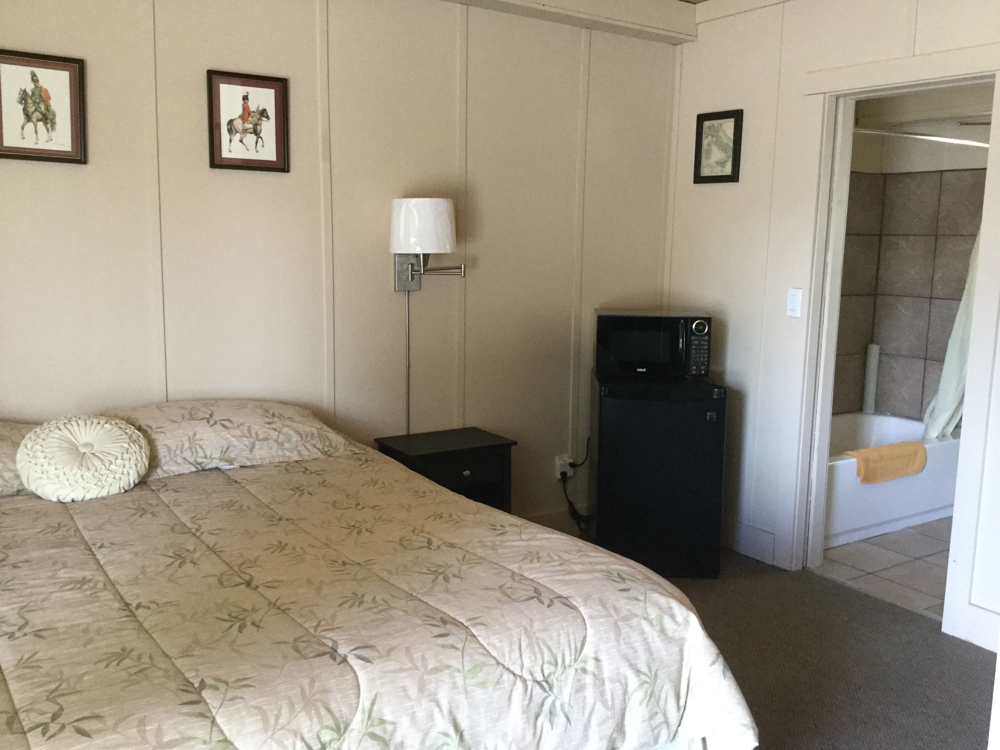 Un dormitorio con cama, mesita de noche, microondas y puerta que da a un baño.