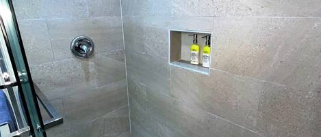 A modern shower with a glass door, a built-in shelf with toiletries, and a tiled floor.